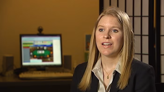 Foto einer blonden Autorin in dunklem Blazer, die in einem Büro vor einem Computerbildschirm sitzt